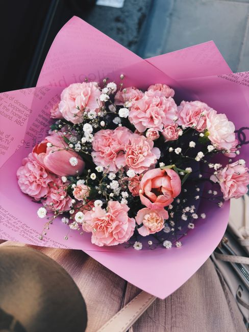 A bouquet of fresh pink flowers, including carnations, tulips, and spray roses, arranged in a tightly packed floral display. The flowers feature soft pastel shades with delicate, ruffled petals and sm